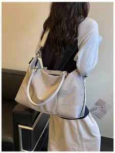Large beige travel tote bag with purple bow embroidery shown on shoulder style.