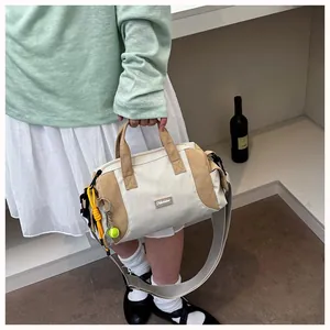 Detailansicht einer khakifarbenen und cremefarbenen Nylontasche, die lässig gehalten wird.