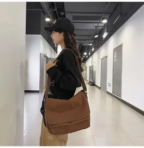Lifestyle view of a large brown canvas messenger bag worn on a shoulder in a hallway