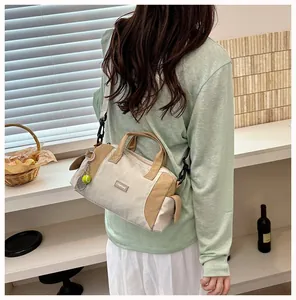 Lässige beige Boston-Umhängetasche mit Tennis-Anhänger an einem Model im grünen Hemd