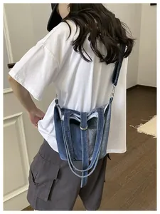 Mannequin portant un sac seau en jean bleu comme sac à bandoulière dans une pièce.