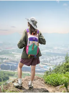 Wanderin auf einem Berg mit buntem Outdoor-Rucksack und Blick auf die Stadtlandschaft.