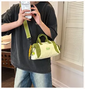 Modell trägt eine sportliche cremefarbene und grüne Barrel-Tasche mit Tennisball-Anhänger