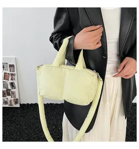 Detail view of a stylish light yellow puffer tote bag held by a model in a black jacket