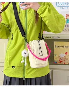 Detail view of the cream-colored crossbody phone bag with vibrant pink handle and fuzzy charm