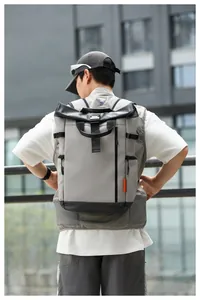 Grey water-resistant roll-top backpack shown on a male model in an urban outdoor setting