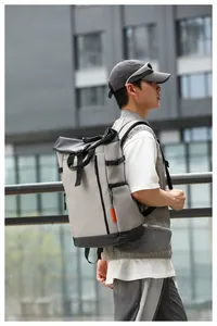 Side view of a gray and black waterproof roll-top backpack on an Asian male model