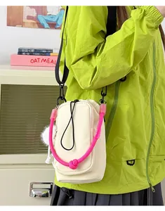 Detailed view of cream crossbody phone bag with bright pink rope handle and keychain detail.