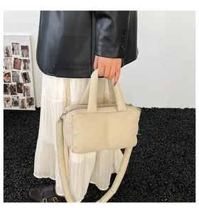 Detailed view of a cream padded puffer handbag held by a person in casual outfit