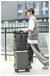 Large roll-top backpack placed on top of a silver rolling suitcase for travel