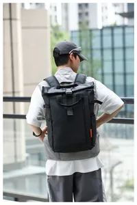 Back view of a man carrying a black water-resistant roll-top backpack outdoors.