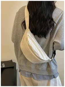 Rear view detail of a cream-colored crescent sling bag worn casually over a grey sweatshirt