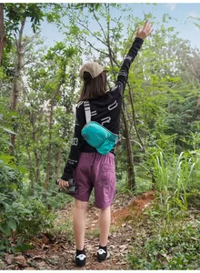 Frau mit türkisfarbener Outdoor-Gürteltasche beim Wandern auf einem Waldweg.