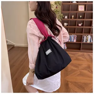 Detail view of a large black drawstring shopper bag with pink straps worn by an Asian model.