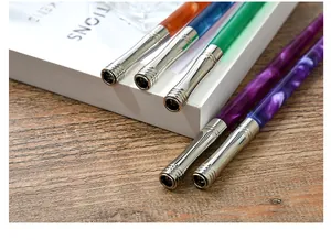 Close-up of colorful resin dip pens with polished silver-toned metal ferrules on a desk.