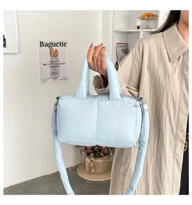 Detailed view of a light blue quilted puffer tote bag being held in a stylish indoor setting