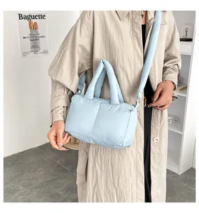Light blue puffy quilted shoulder bag worn with a beige trench coat for a trendy look.