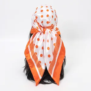 Close-up detail of a vibrant orange polka dot silk scarf worn as a stylish headscarf.