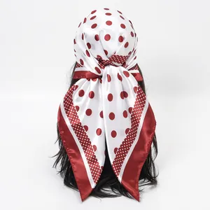 Close-up of a red and white polka dot silk scarf styled as a headscarf on a model.