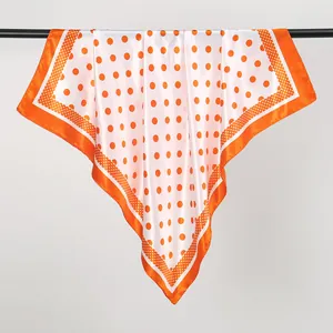 Close-up detail of a large orange polka dot silk scarf with elegant satin texture