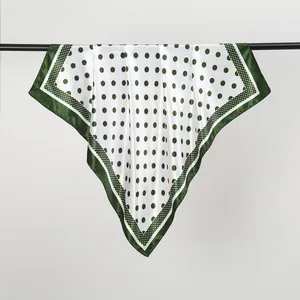 Detail of green polka dot silk scarf hanging on a display rod with white background