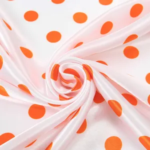 Close-up view of the smooth texture and vibrant orange polka dot pattern of this silk scarf.