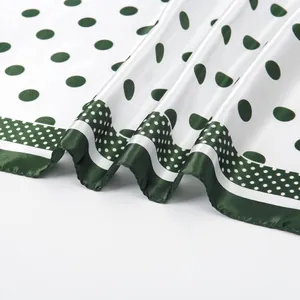 Detail view of smooth silk scarf featuring green polka dots on white background