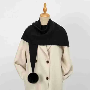 Dettaglio di uno scialle in maglia nera con pompon decorativo in pelliccia su un manichino.