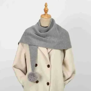 Dettaglio di sciarpa grigia a maglia con pompon decorativo su un cappotto color crema elegante