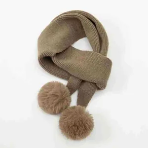 Vista dettagliata di una morbida sciarpa in maglia marrone con pompon in ecopelliccia per l'inverno.