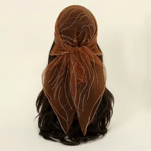 Detail view of a brown polyester headscarf featuring elegant rhinestone wave patterns.