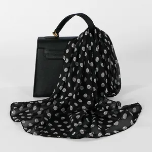 Detail of black chiffon long scarf with white polka dots draped over a black bag