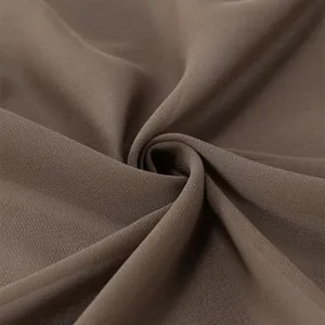 Vue détaillée de la texture du tissu en mousseline marron montrant son drapé doux et mat