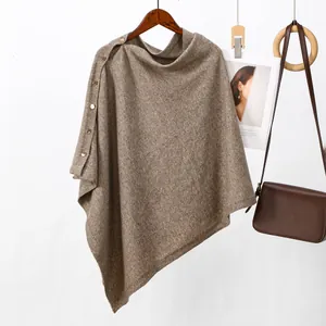 Macro detail of brown knitted poncho featuring stylish gold buttons and soft wool-like texture.