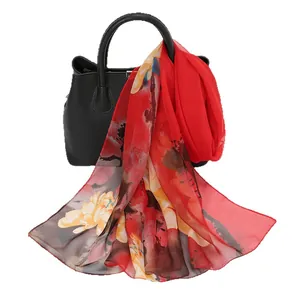 Elegant red floral print chiffon scarf draped over a black handbag for fashion display