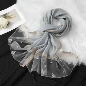 Détail d'une écharpe élégante en organza gris avec broderie papillon et perles