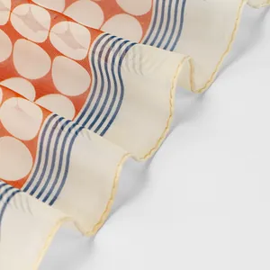 Close-up of lightweight chiffon scarf with orange polka dots and blue wavy patterns.
