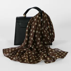 Elegant brown chiffon scarf with green polka dots draped over a black bag
