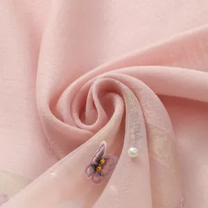 Détail macro d'une écharpe en organza rose avec broderie papillon et perles nacrées