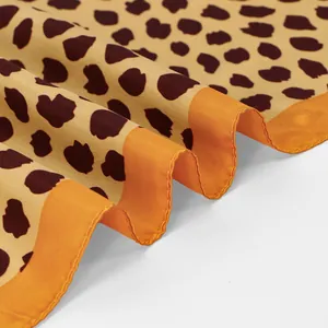 Gros plan d'un foulard en satin léopard montrant la texture lisse et l'ourlet orange