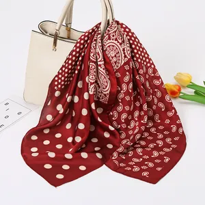 Detailed view of a red paisley and polka dot silk scarf draped on a white handbag with tulips