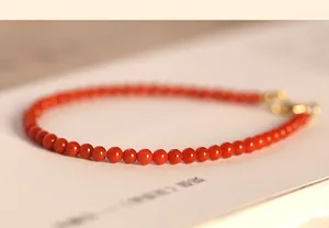 Macro detail showing tiny red agate beads and a delicate gold clasp on a bracelet