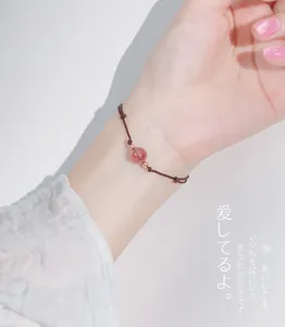 Detailed close-up showing a delicate strawberry crystal bead on a brown hand-woven cord bracelet