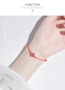 Close-up of a hand-woven red cord bracelet with a translucent strawberry crystal bead