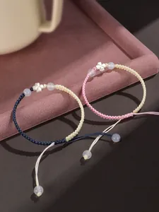 Vue détaillée de bracelets trèfles tressés à la main avec breloques argent et perles blanches.