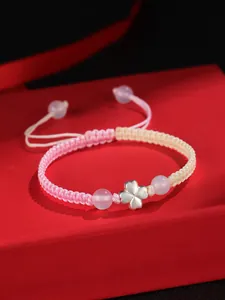 Gros plan d'un trèfle à quatre feuilles en argent 925 sur un bracelet rose tressé.