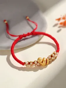 Gros plan d'un bracelet tressé rouge avec breloque serpent dorée et nœuds