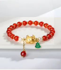 Detailopname van rode agaat armband met gouden drakenbedeltje en parelaccenten