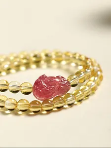 Gros plan d'une breloque en quartz fraise sur un bracelet en quartz rutilé doré.