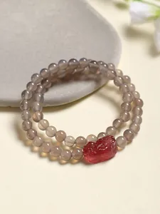 Gros plan d'un bracelet double en agate grise avec une breloque en quartz fraise rouge.